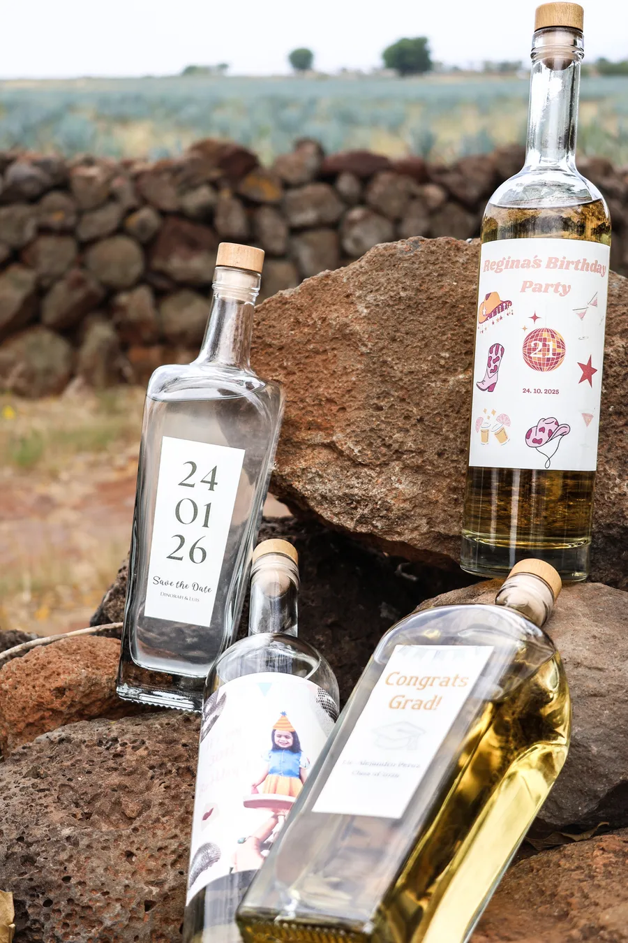 Cuatro botellas personalizadas sobre piedra volcánica frente a un campo de agave azul
